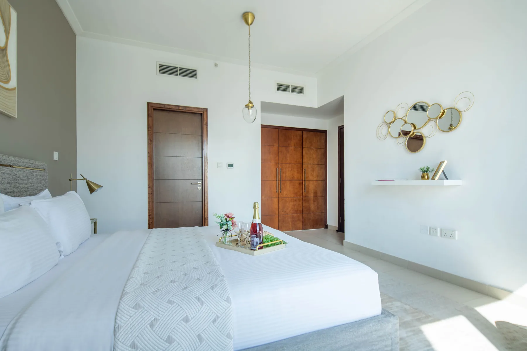 Un dormitorio luminoso con una cama blanca, puertas de madera y espejos decorativos.