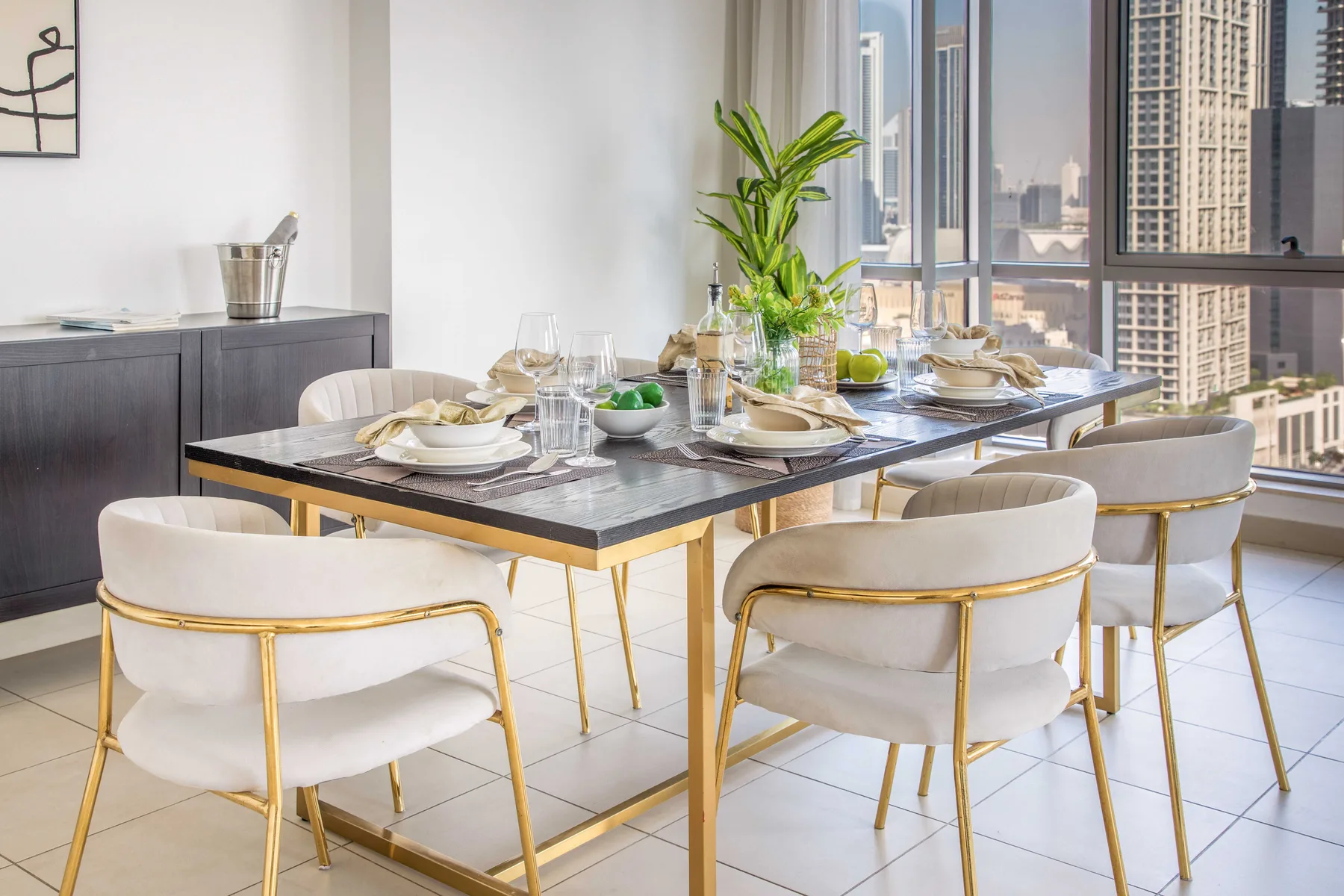 Comedor con una mesa puesta junto a grandes ventanas con vistas a edificios de la ciudad.