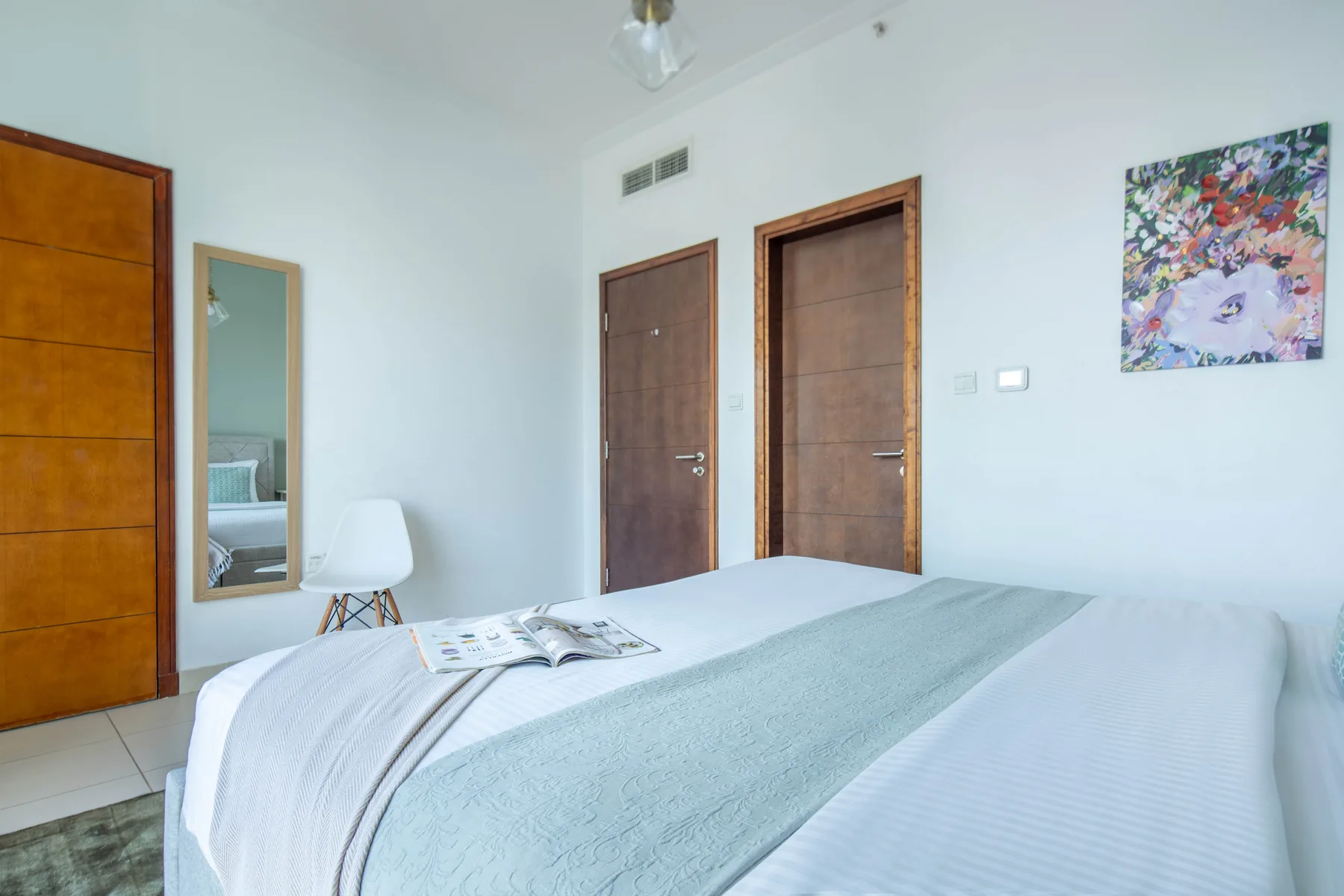 Un dormitorio luminoso con una cama bien tendida y arte colorido en la pared.