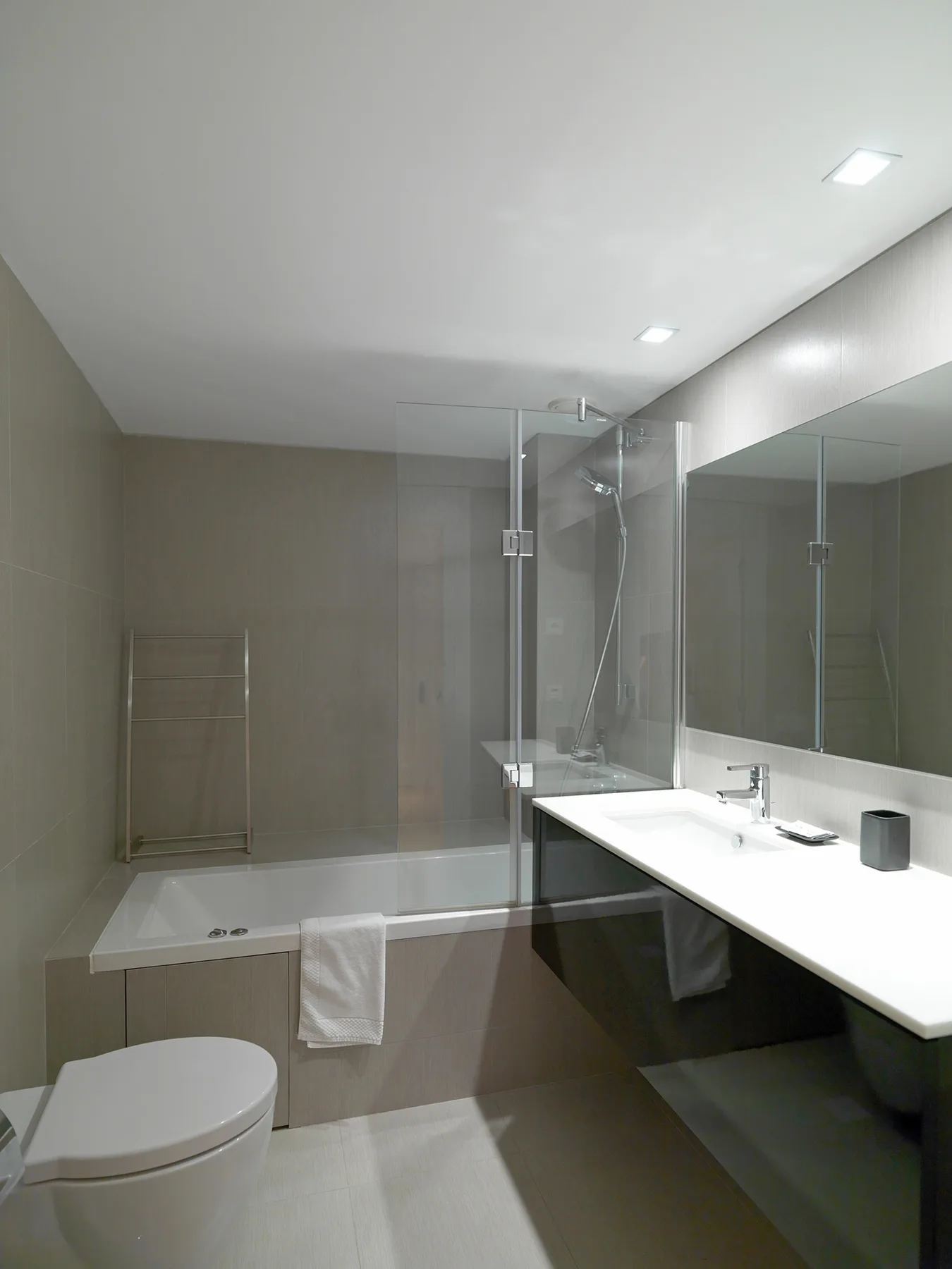 A modern bathroom with a bathtub, glass shower screen, and long sink counter.