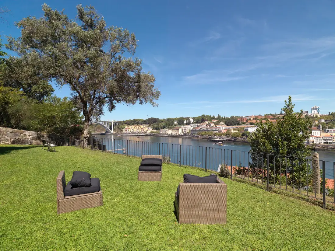 A grassy riverside seating area overlooks the water and buildings across the river.