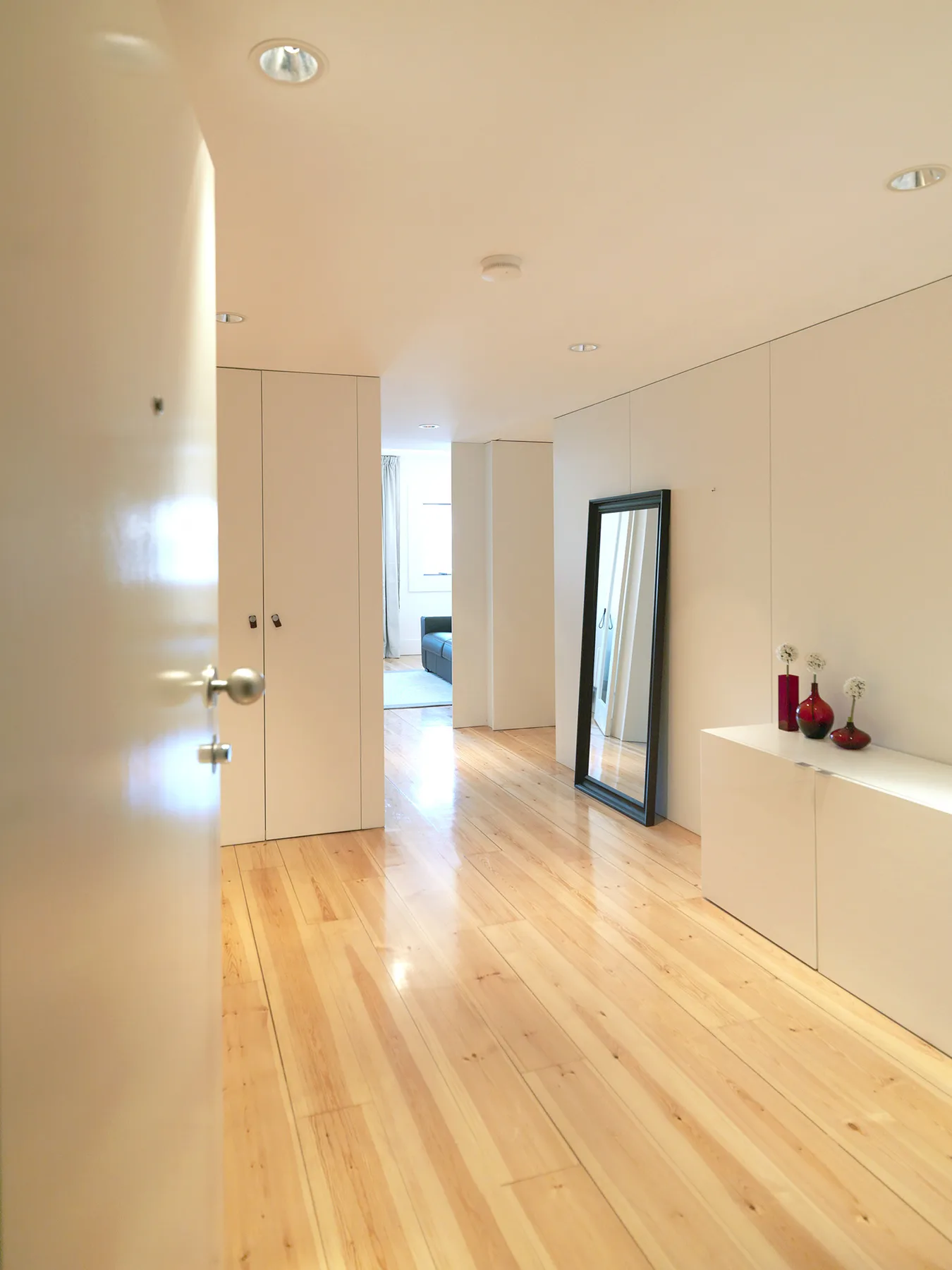 A bright hallway with light wood flooring and a full-length mirror.
