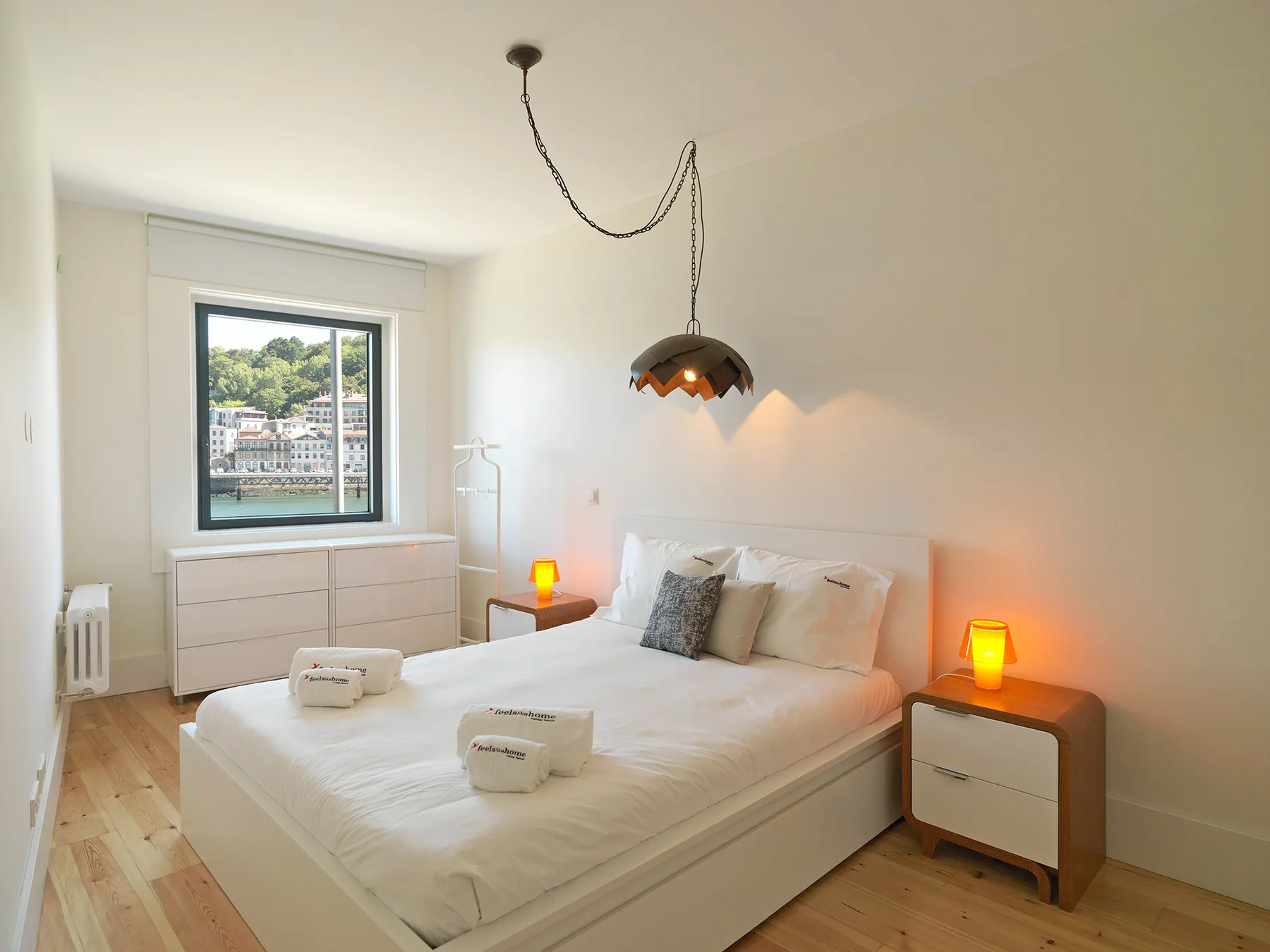 A bright bedroom with a bed and a window overlooking the waterfront.