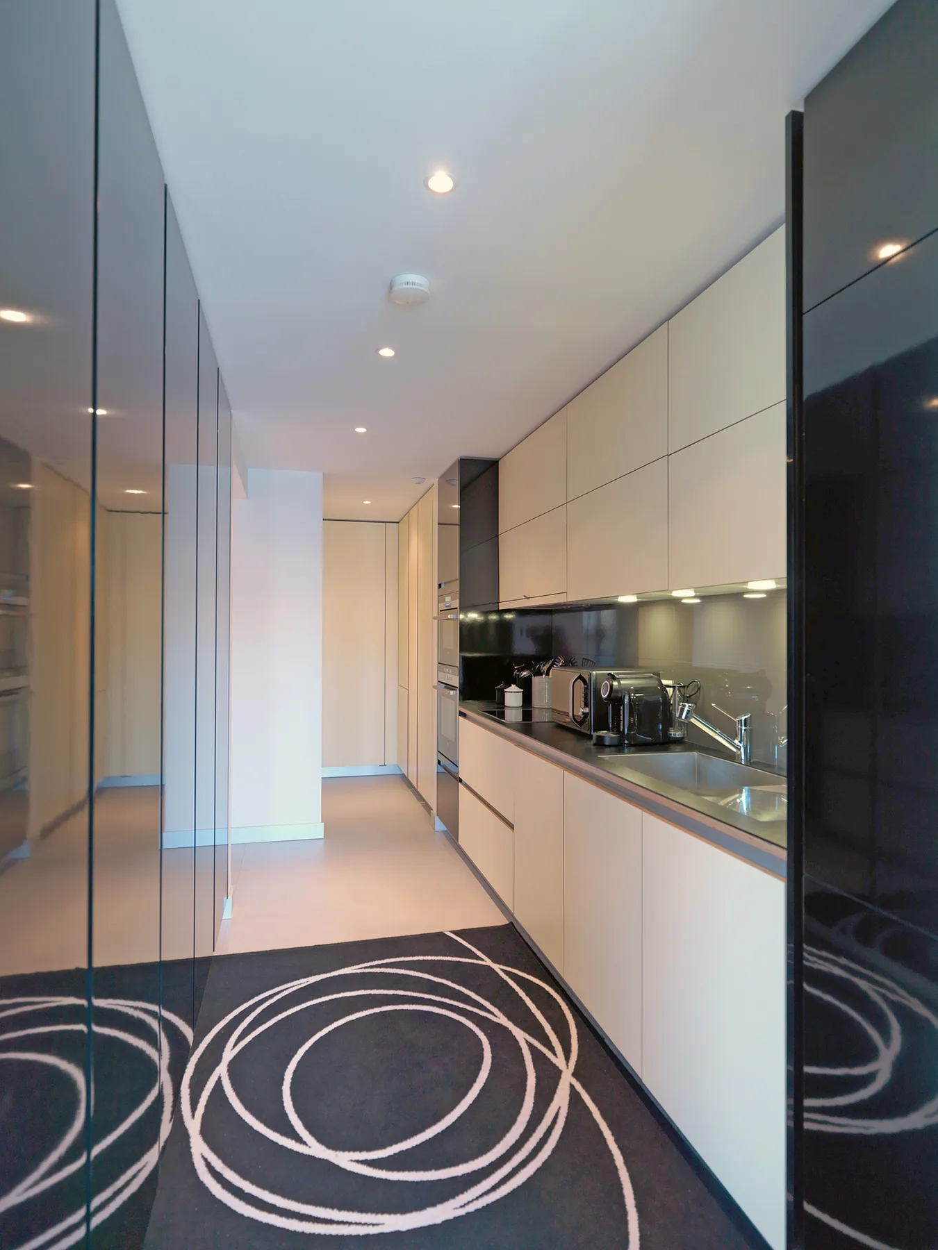 A modern kitchen with light cabinets, dark countertops, and a patterned rug.