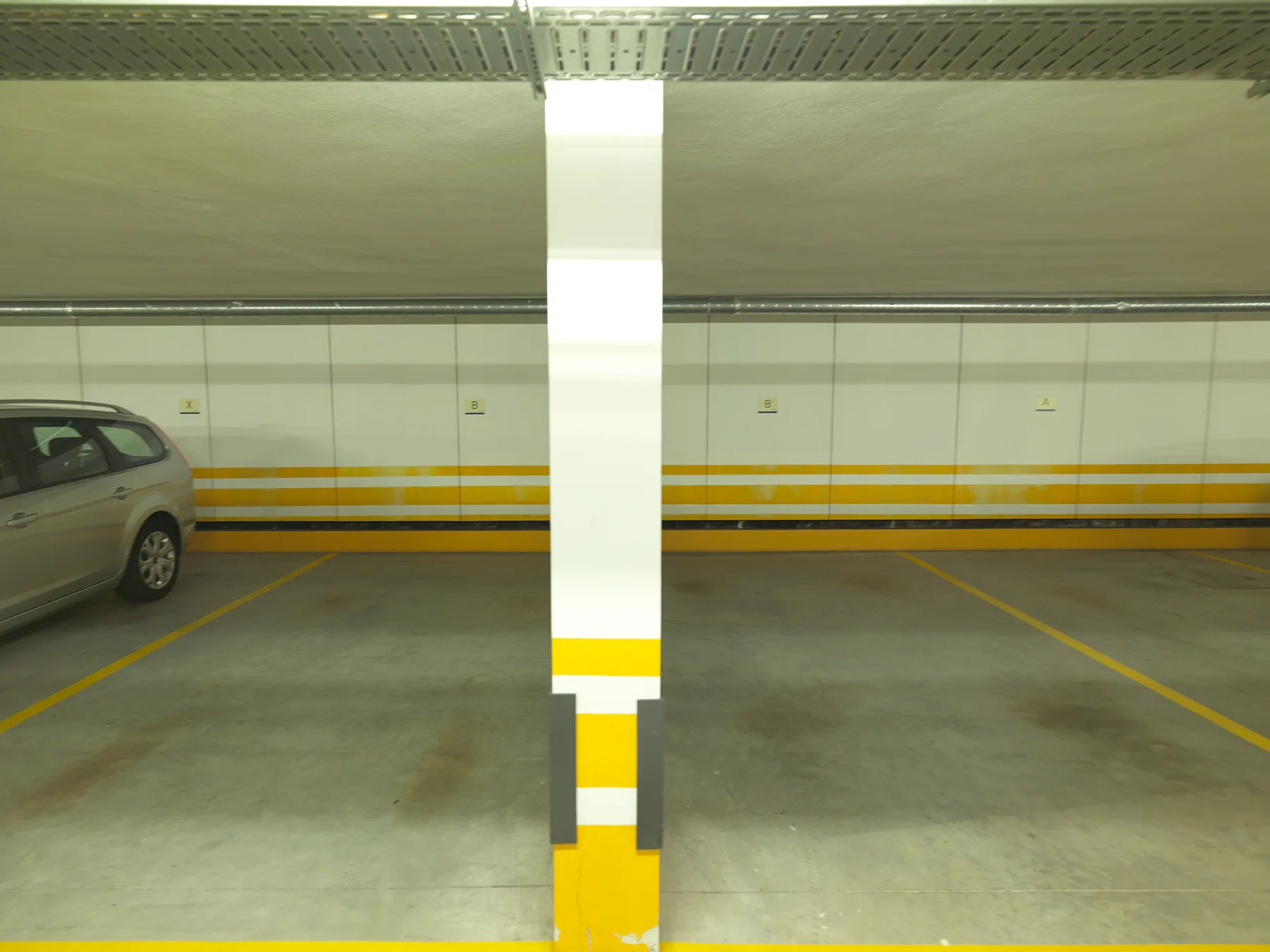 An indoor parking garage with marked spaces and a parked car.