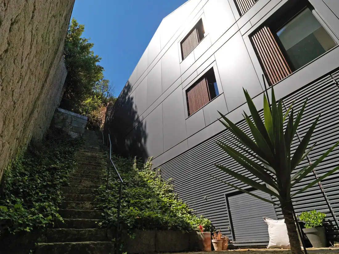 A modern building borders a narrow outdoor stairway lined with greenery.