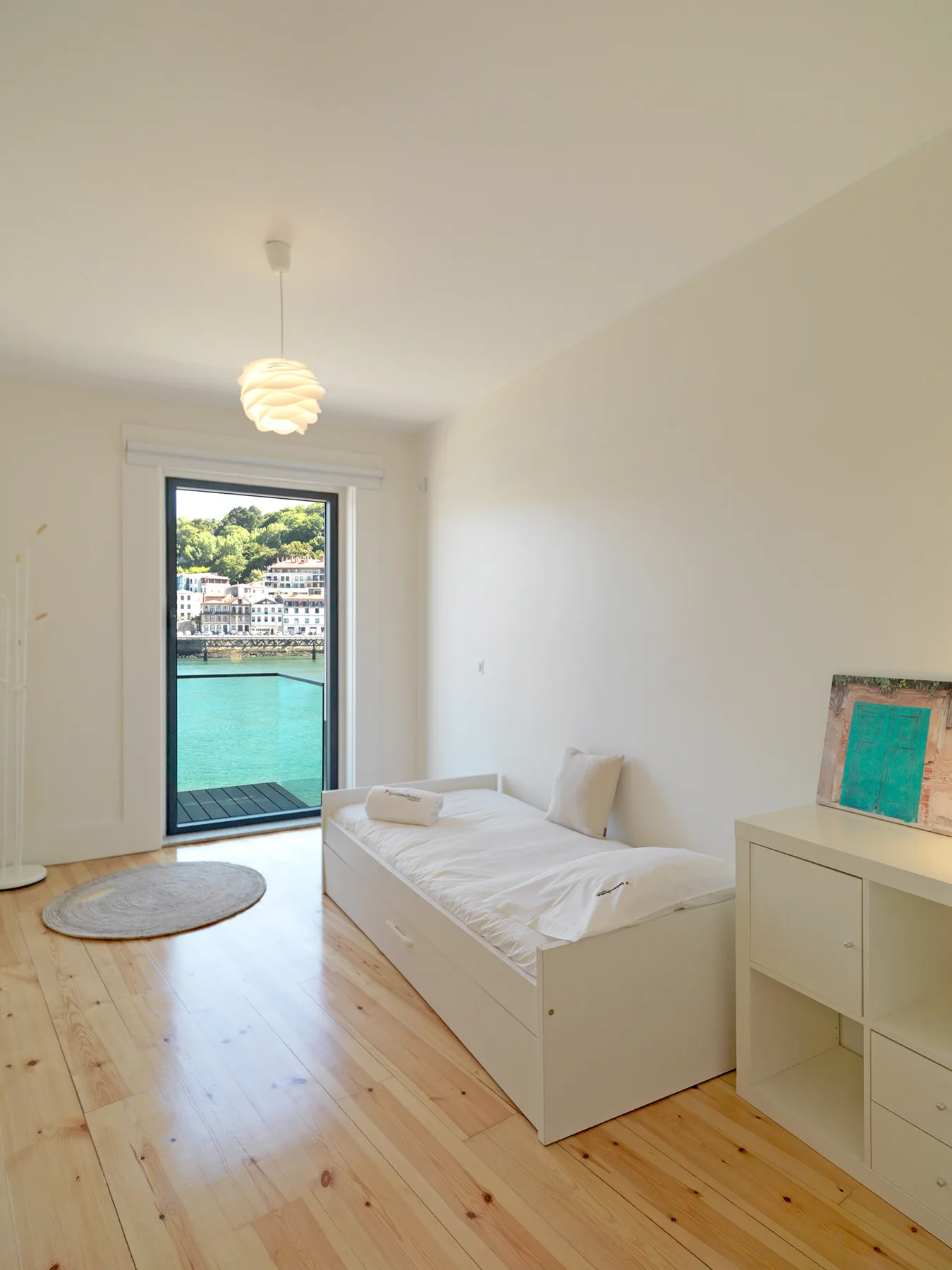 A bright bedroom with a bed beside a glass door overlooking the water.