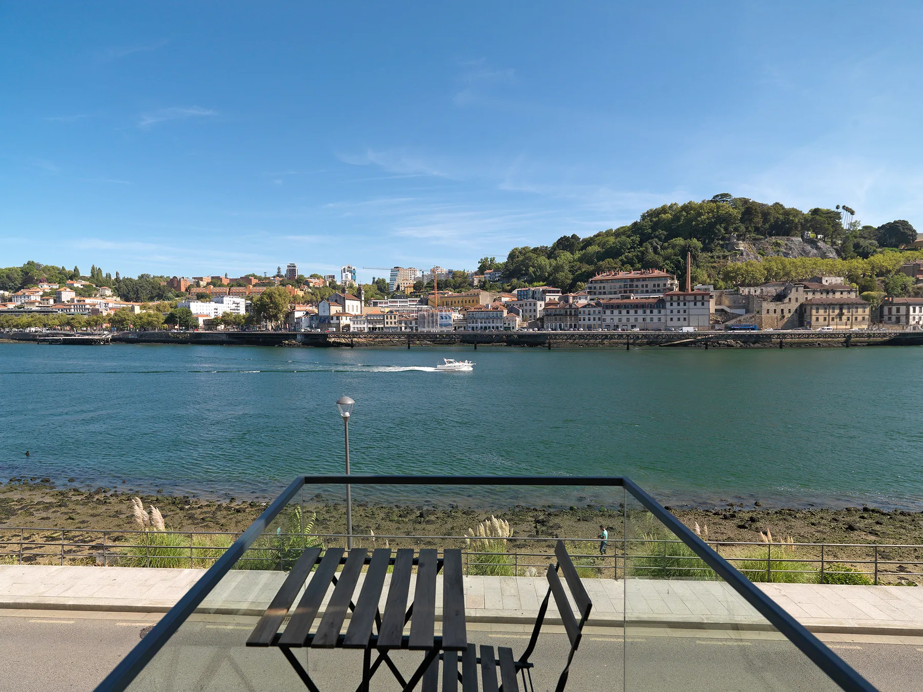 A riverside terrace overlooks the water and the hillside buildings across the river.