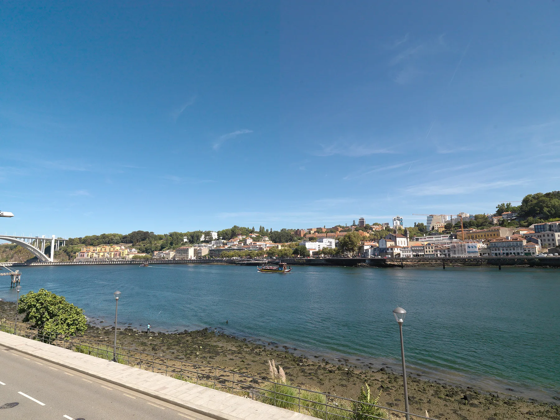 A riverside view across the water toward a city waterfront and hillside buildings.