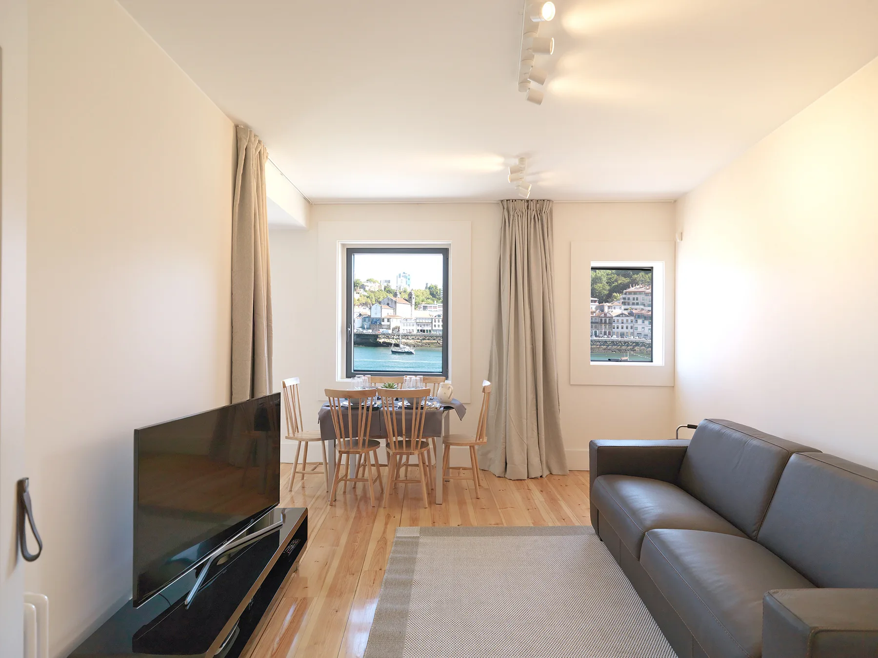 A living and dining area with a gray sofa and windows overlooking the water.
