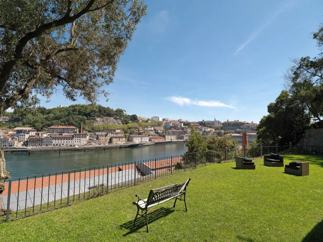 A grassy riverside garden overlooks the water and buildings on the opposite bank.
