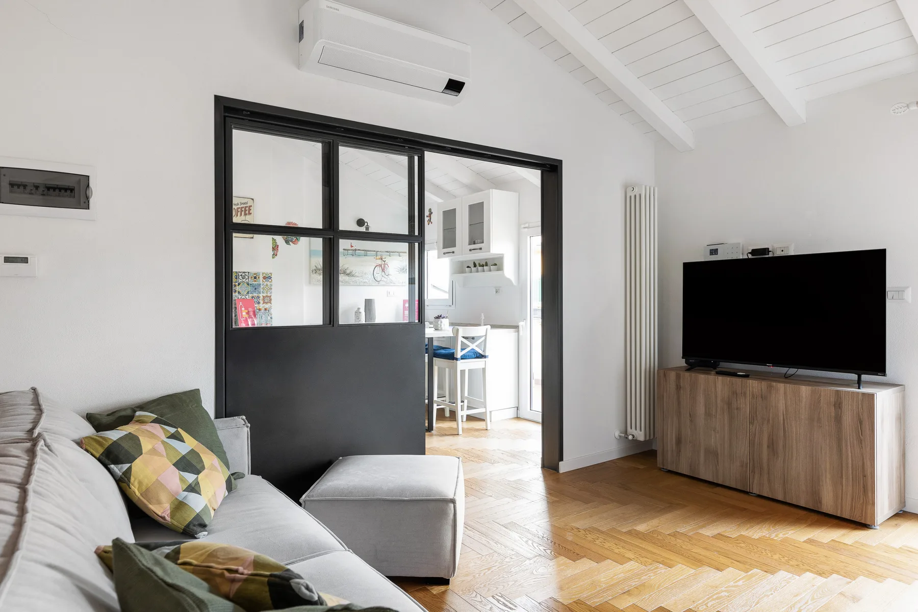 Una sala luminosa con asientos y un televisor junto a una mampara de vidrio.