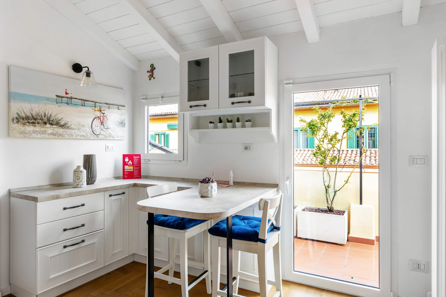 A bright kitchen with white cabinetry, a dining table, and an open glass door to a terrace.