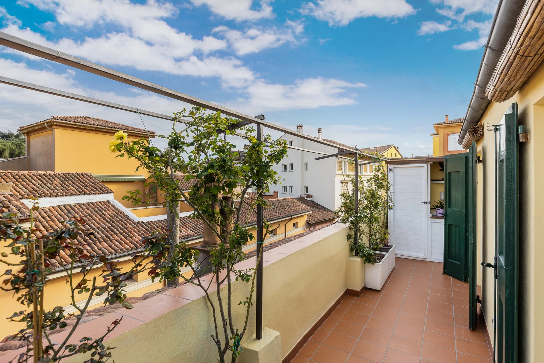 Una terraza con suelo de baldosas y plantas en macetas da a tejados cercanos.