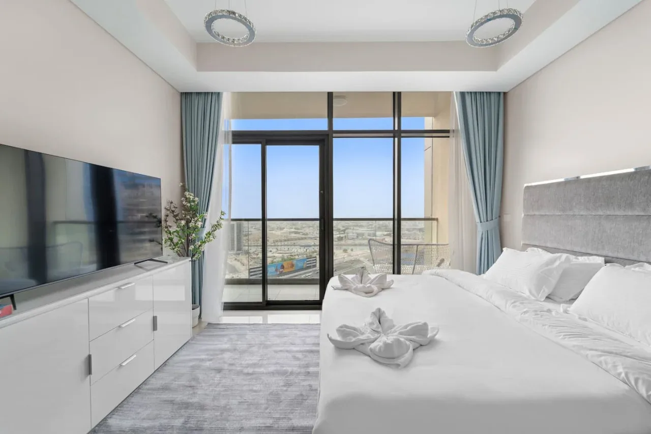 A bright bedroom with a large bed beside floor-to-ceiling windows.