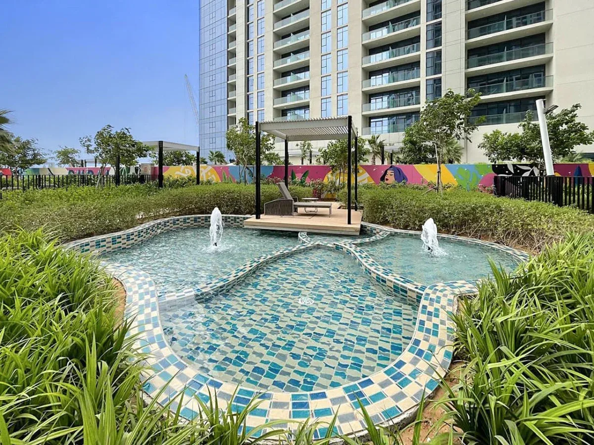 An outdoor tiled pool sits beside landscaped greenery and a shaded seating area.