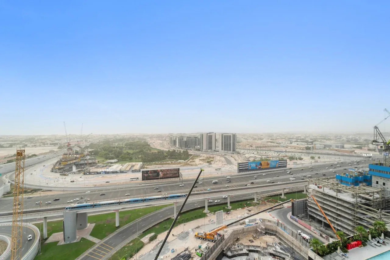 A wide city view shows highways, construction sites, and distant buildings beneath a clear sky.