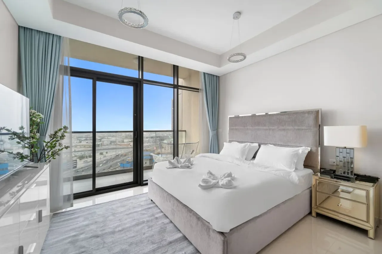 A bright bedroom features a large bed beside floor-to-ceiling windows.