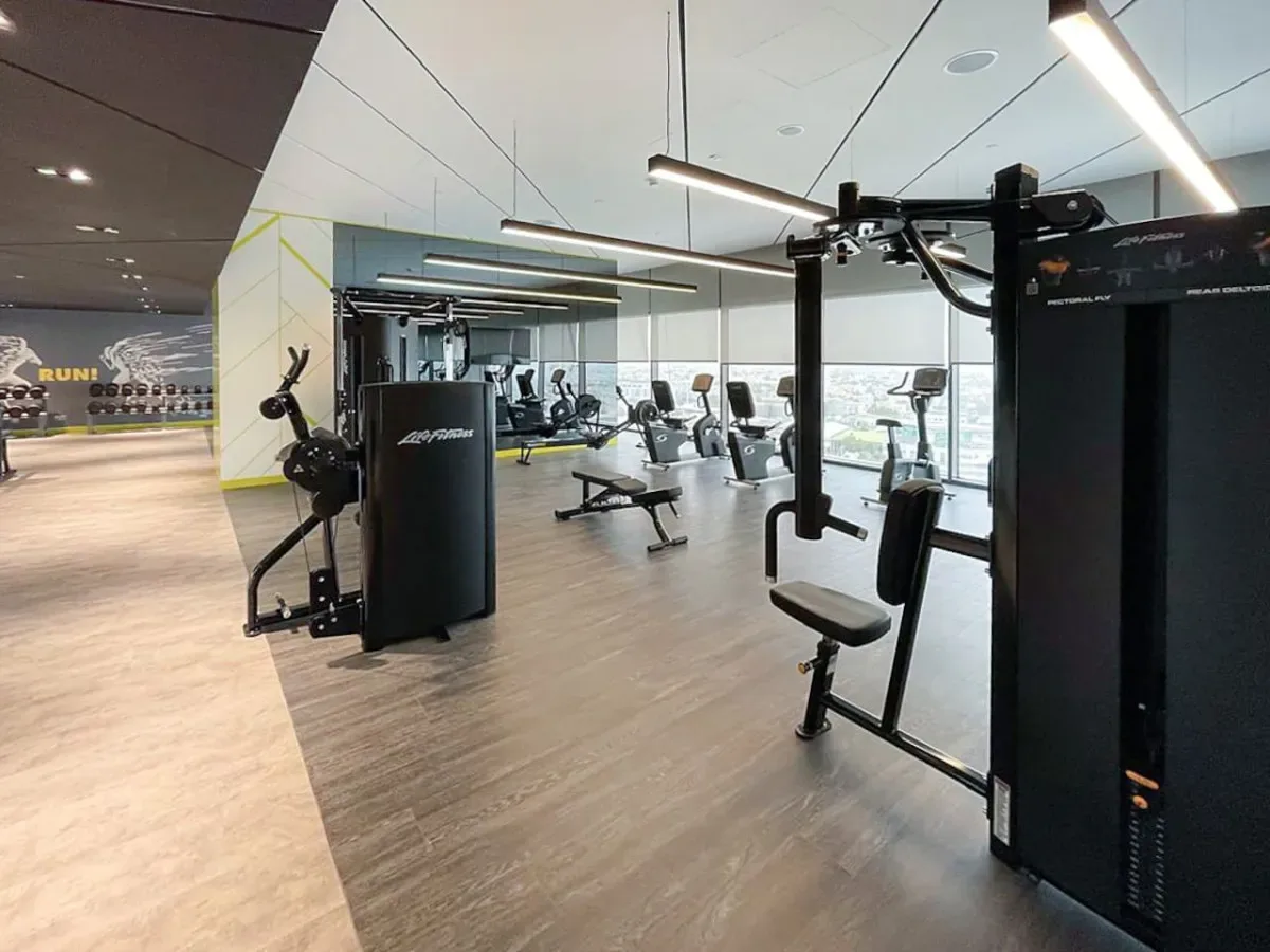 A gym with weight machines and exercise equipment beside large windows.