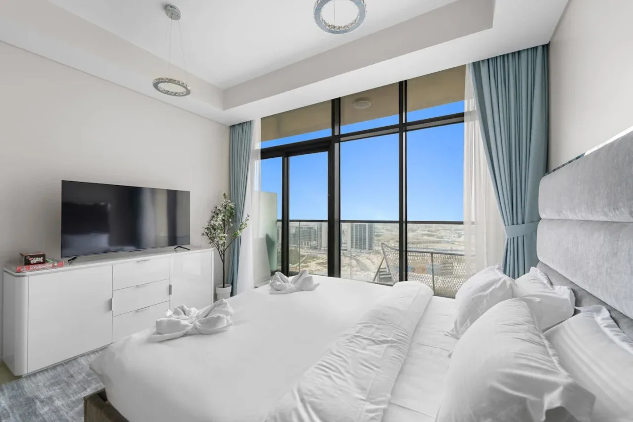 A bright bedroom with a large bed beside floor-to-ceiling windows.