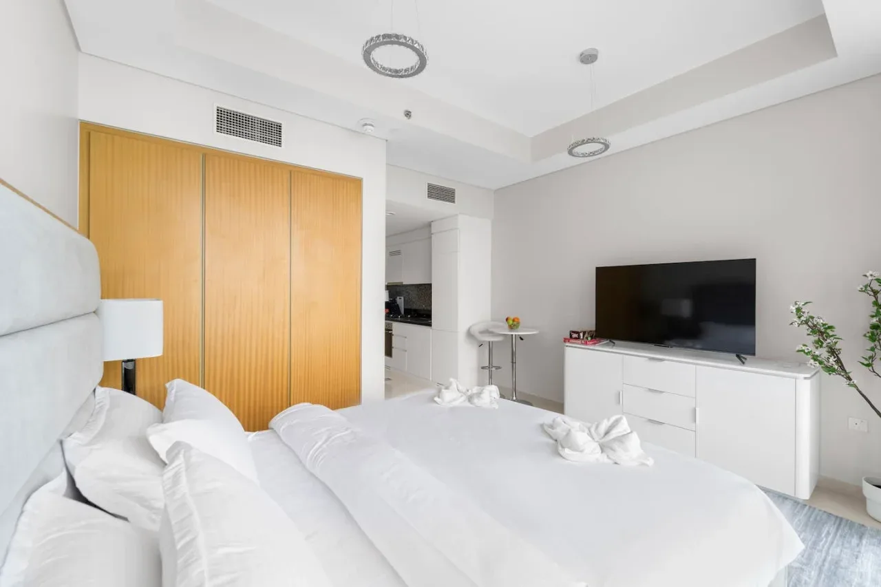 A bright bedroom with a bed, wooden wardrobes, and a television on a cabinet.