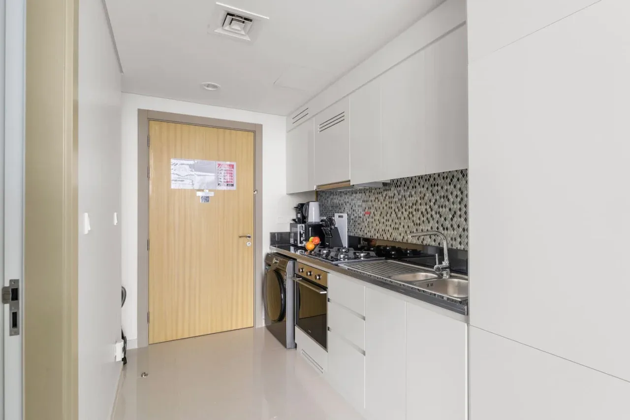 A compact kitchen with white cabinets, a cooktop, and a patterned backsplash.