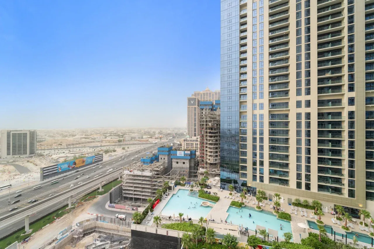 High-rise buildings overlook a swimming pool and a busy highway.