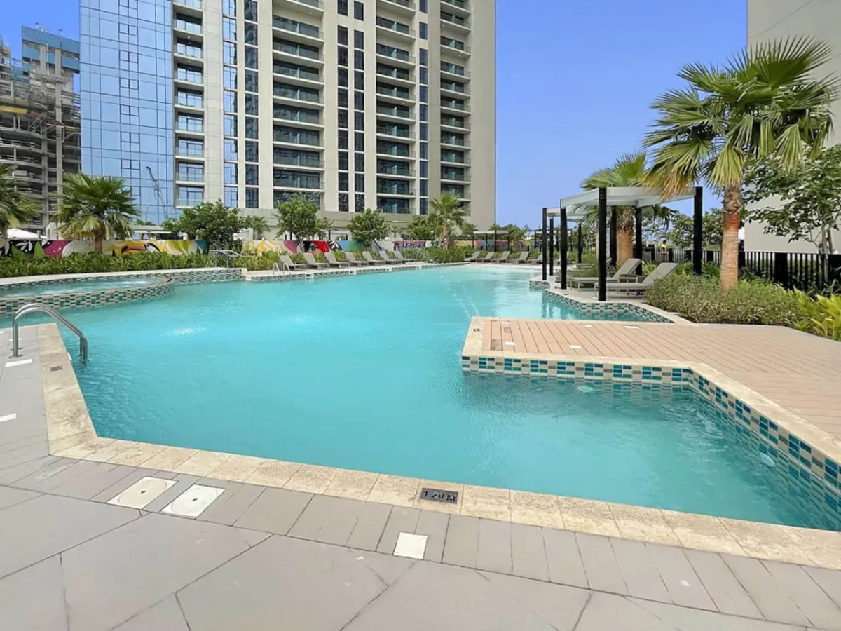 A swimming pool beside a high-rise building, with palm trees along the deck.