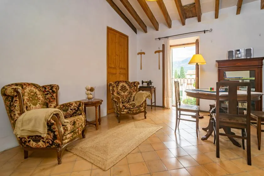 A living room with patterned seating, a wooden dining table, and an open balcony door.