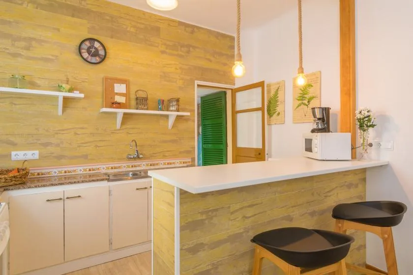 A warm-toned kitchen with a long counter, sink, and two stools.
