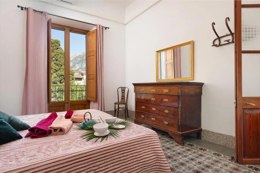 A bedroom with a striped bedspread, wooden dresser, and open window.