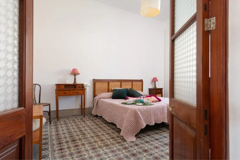 A bedroom with a bed, bedside tables, and patterned tile flooring.