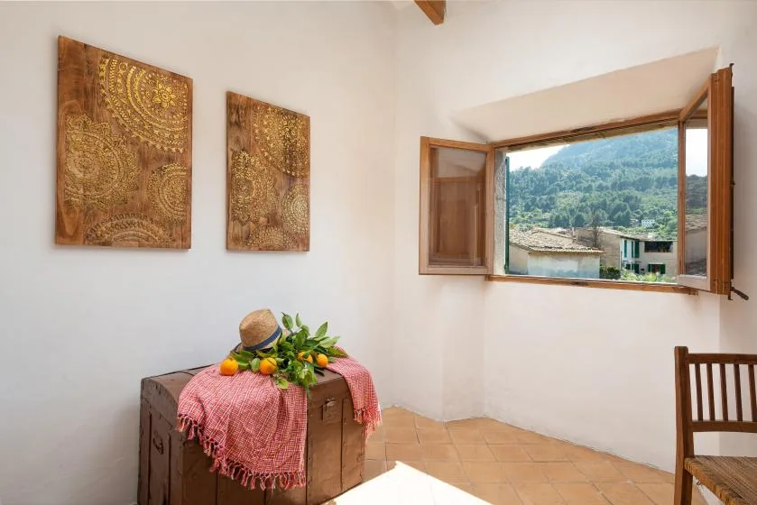 A bright room with patterned wall art, a wooden chest, and an open window overlooking green hills.
