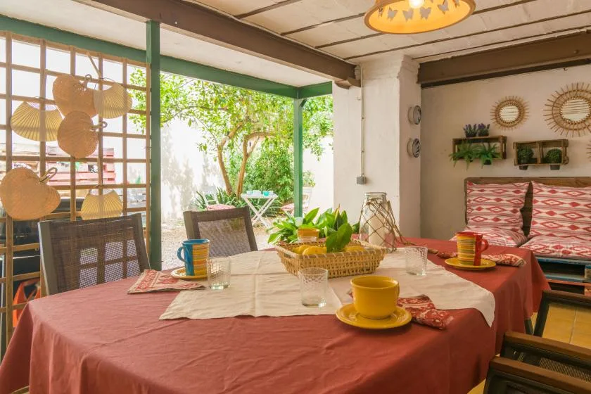 A dining area with a long table set with cups and dishes beside an open garden view.
