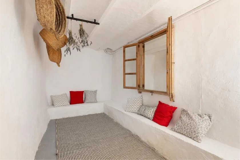 A bright white sitting area with built-in benches, patterned cushions, and an open wooden window.