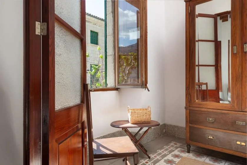 A bright room with open wooden windows and a small table beside the window.