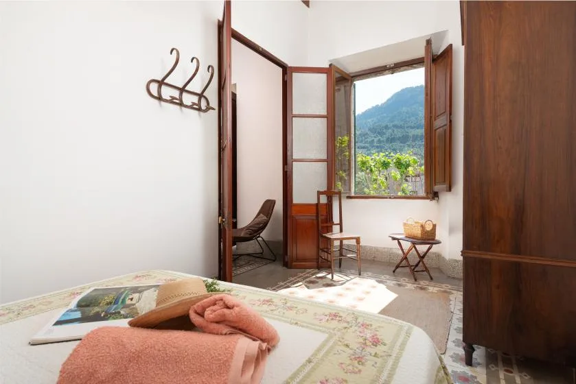 A bedroom with an open window overlooking a green hillside.