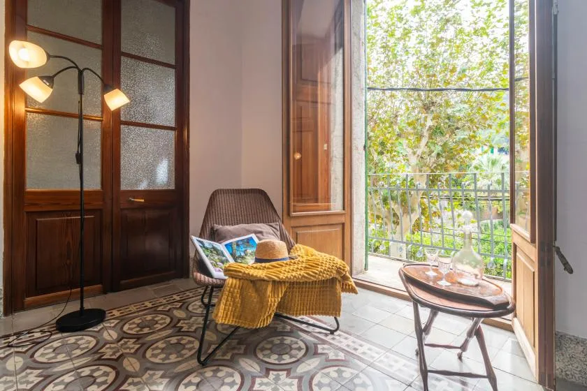 A bright sitting area opens onto a leafy balcony, with a chair and small table.