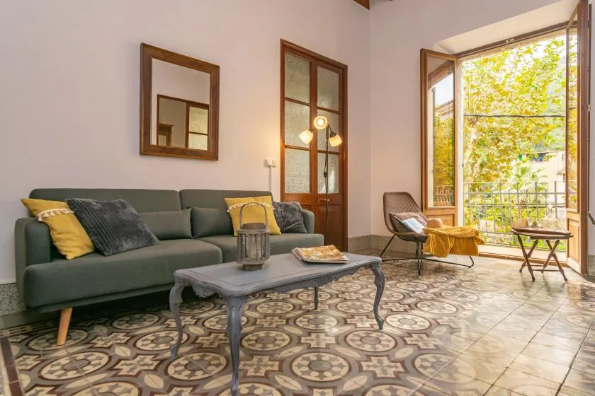 A bright living room with green seating, a coffee table, and an open balcony door.