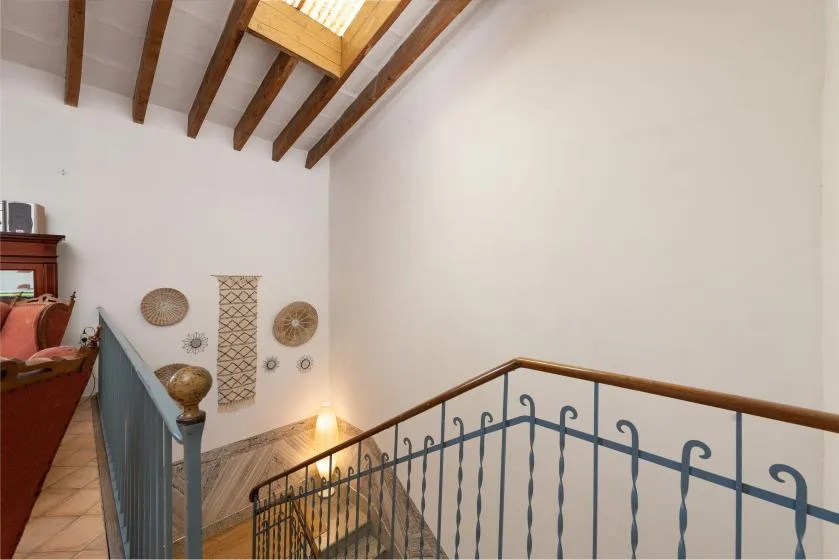 An interior staircase with blue railings sits beneath exposed wooden ceiling beams.