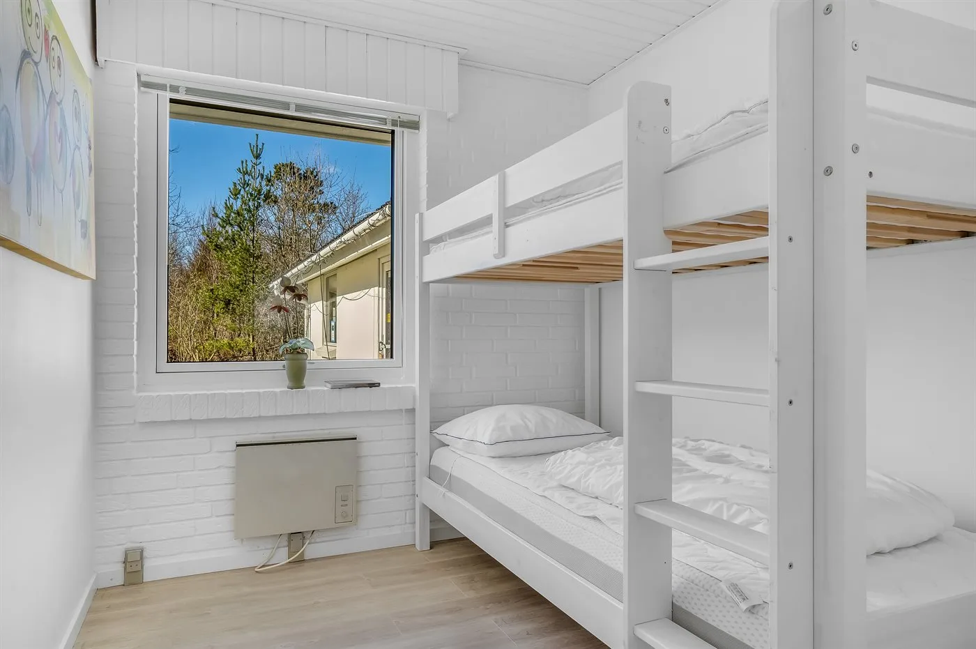 Un dormitorio con literas blancas junto a una ventana con árboles a la vista.