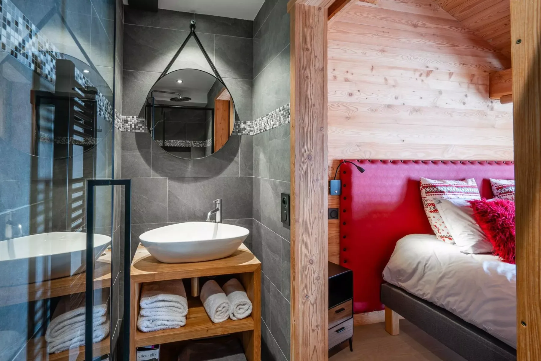 A bathroom with a round mirror and a sleeping area visible through the doorway.