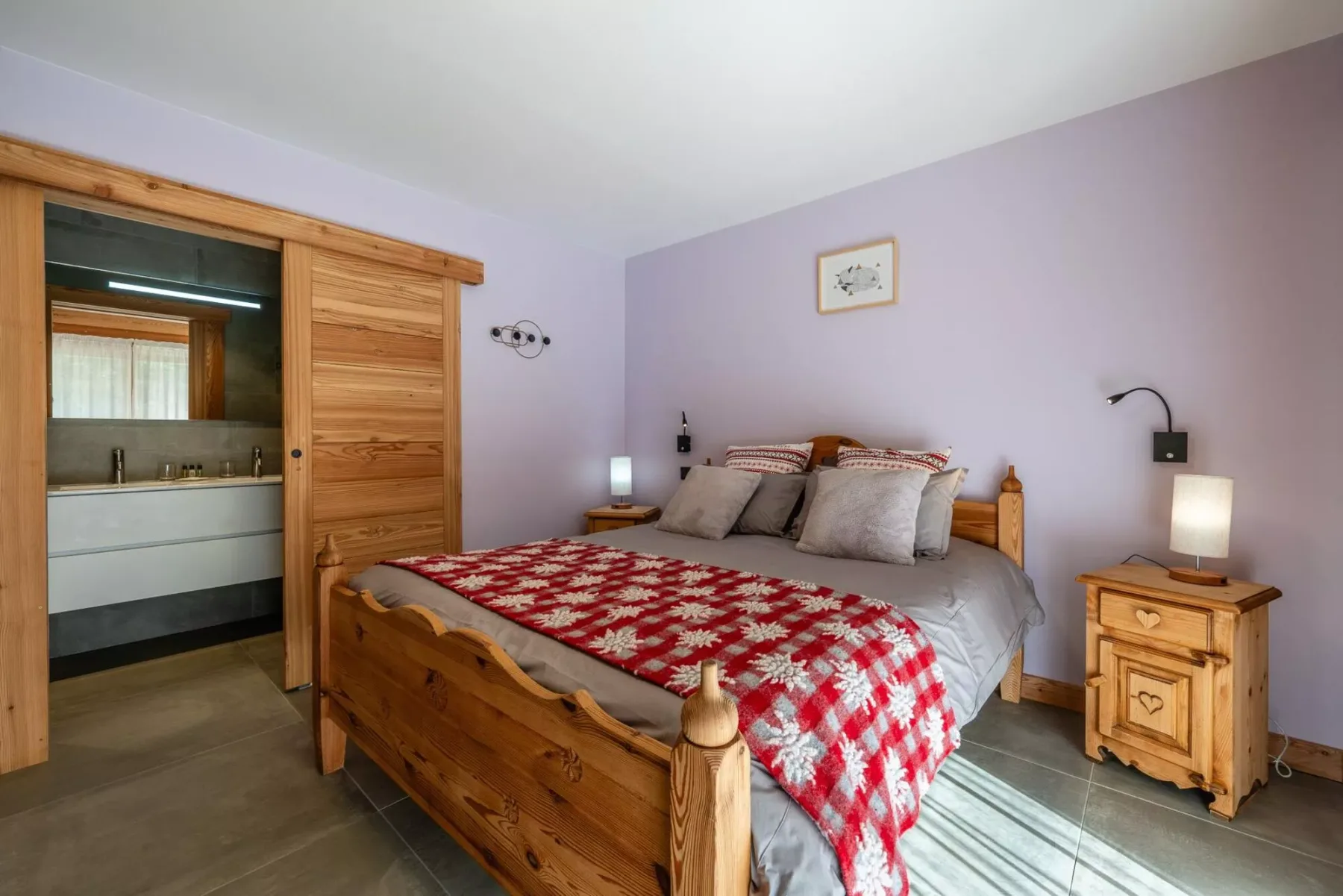 A bedroom with a wooden bed covered by a red patterned quilt.