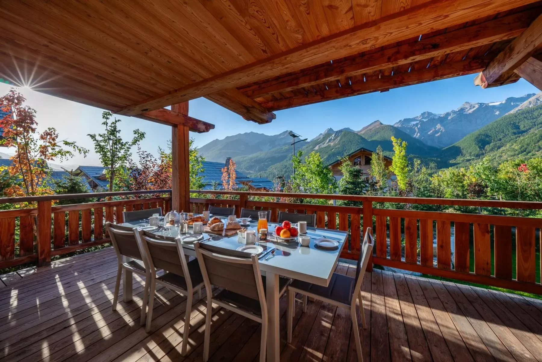 Una zona de comedor al aire libre cubierta tiene vistas a montañas verdes y un valle boscoso.