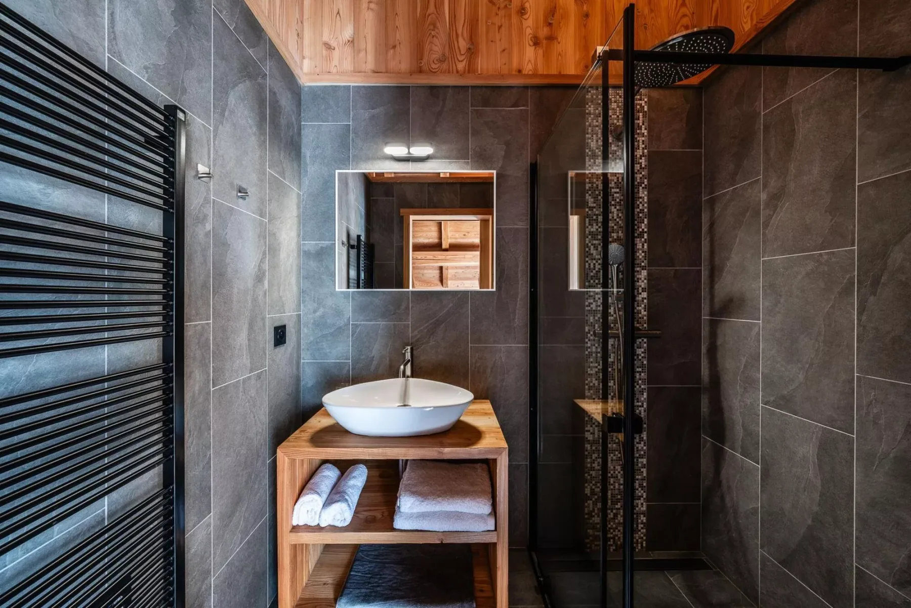 A tiled bathroom features a vanity with a vessel sink and a glass shower.