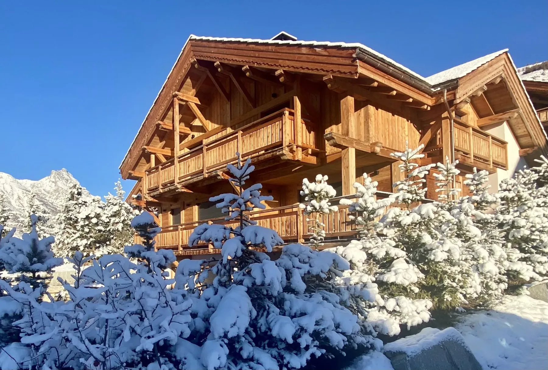 A wooden chalet stands among snow-covered trees beneath a clear blue sky.
