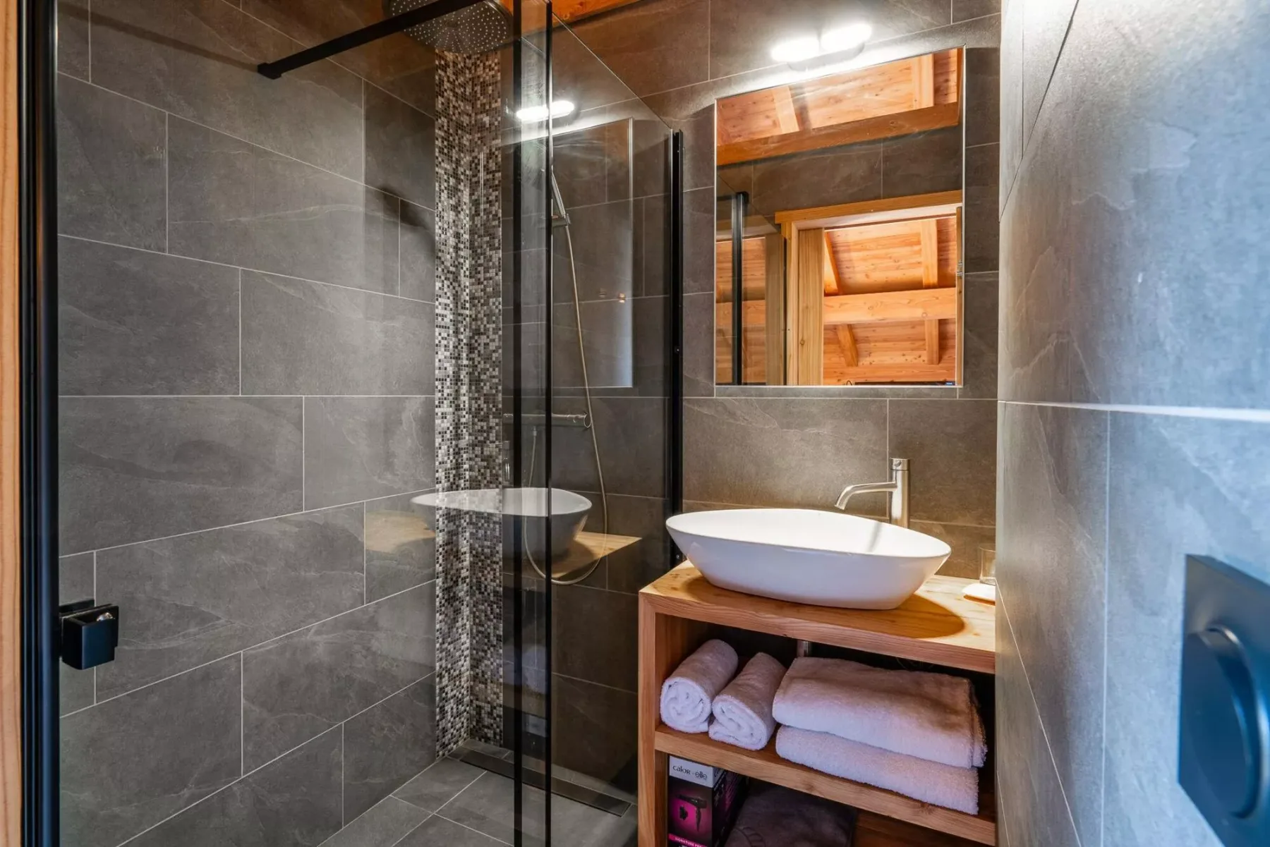 A tiled bathroom with a glass shower and a basin on a wooden vanity.