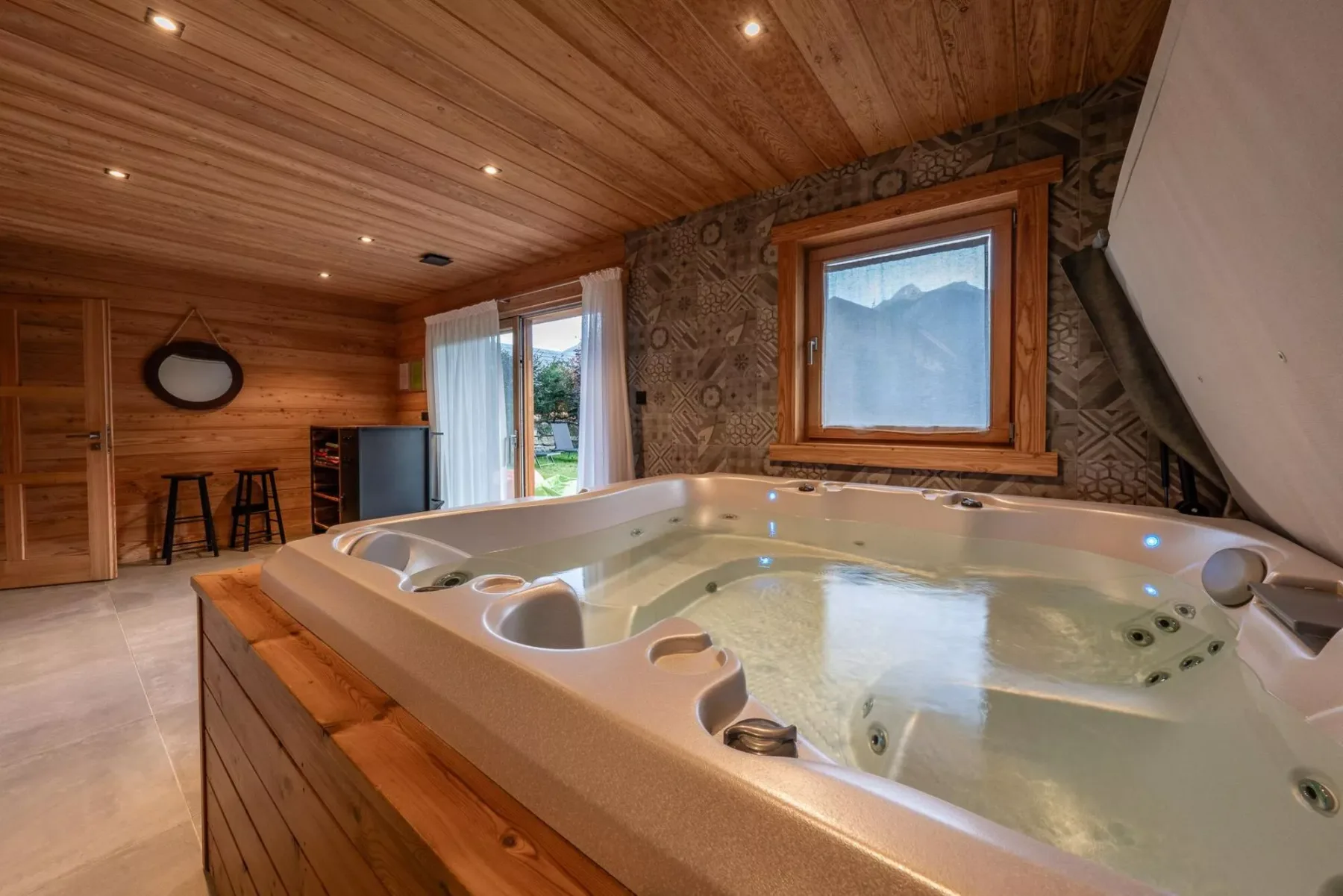 A warm indoor spa room features a large hot tub beneath a wood-paneled ceiling.