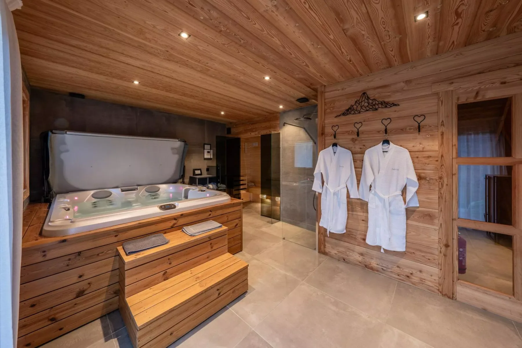 A wood-paneled spa room features a large built-in hot tub and hanging robes.