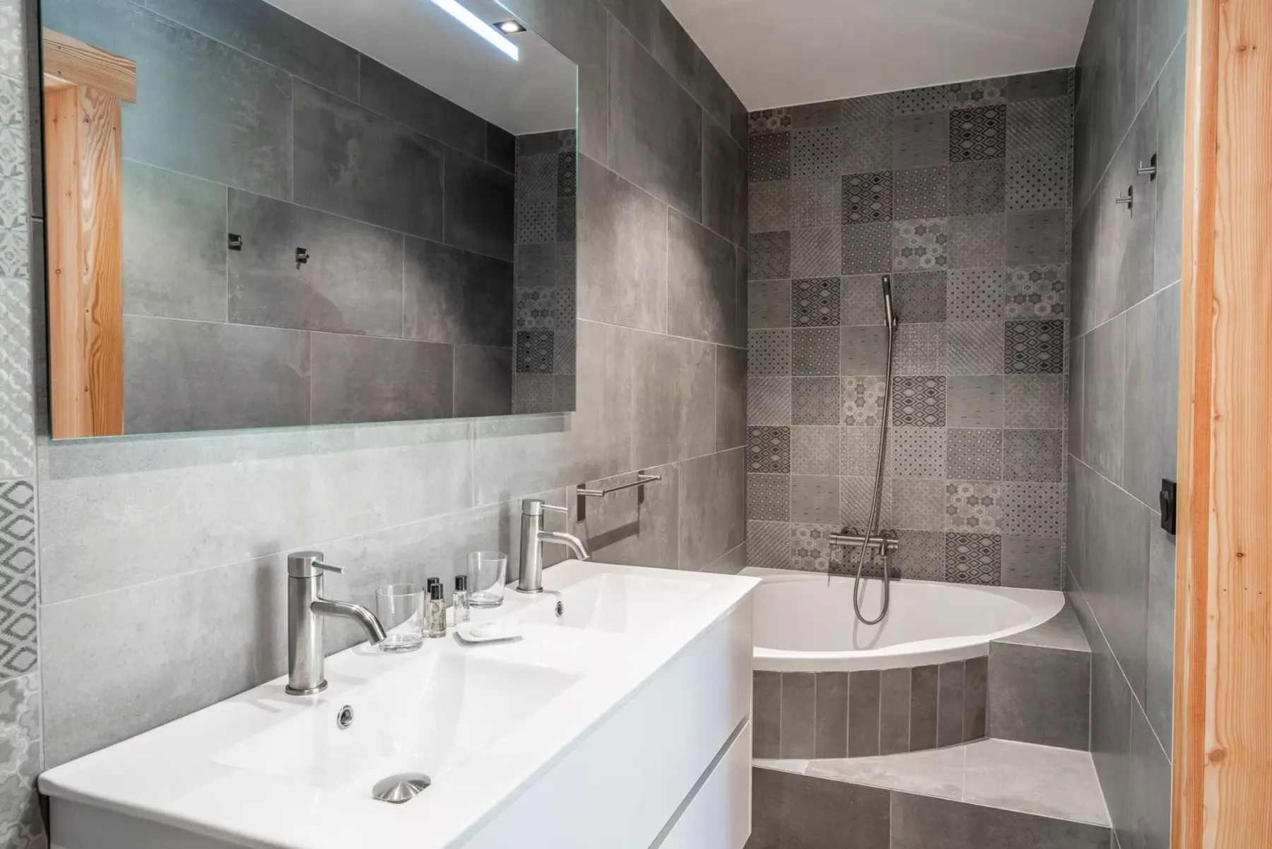 A tiled bathroom with a double sink and a bathtub with a shower.